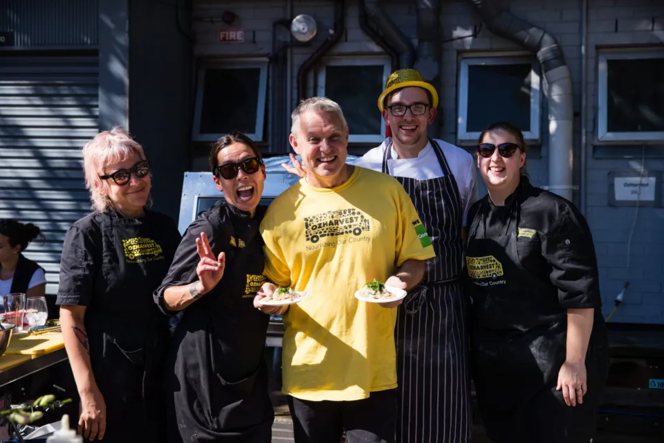 OzHarvest volunteer and kitchen staff smiling.