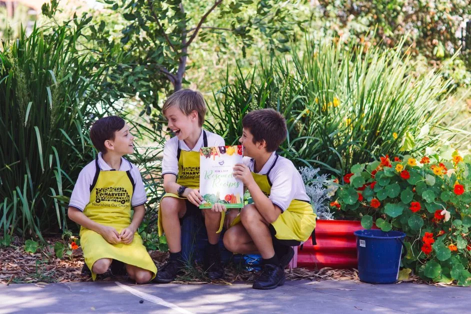 what does OzHarvest do? three FEAST boys holding their FEAST recipe book and wearing ozharvest aprons