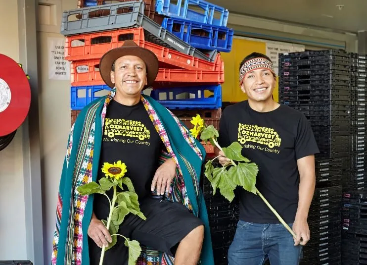 OzHarvest driver Orlando and his son smiling and holding sunflowers in front of crates