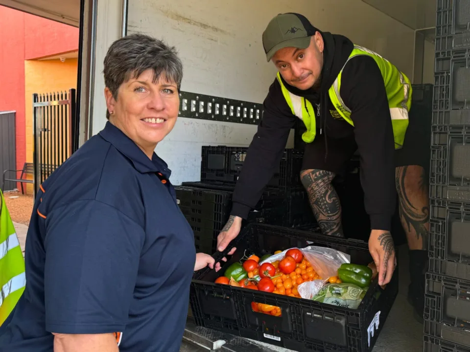 OzHarvest food rescue driver handing a crate of rescued food to a charity partner.